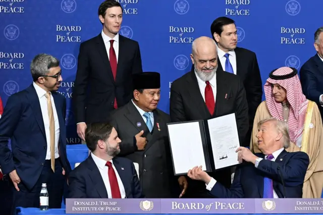 Presiden Subianto berada di tengah pejabat negara lain dalam KTT Dewan Perdamaian. Ia disodorkan sebuah dokumen oleh Presiden AS, Donald Trump yang duduk paling depan.