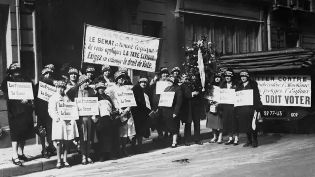 Grupo de mulheres exibindo cartazes em francês, durante a campanha sufragista pelo direito ao voto feminino na França, em 1930
