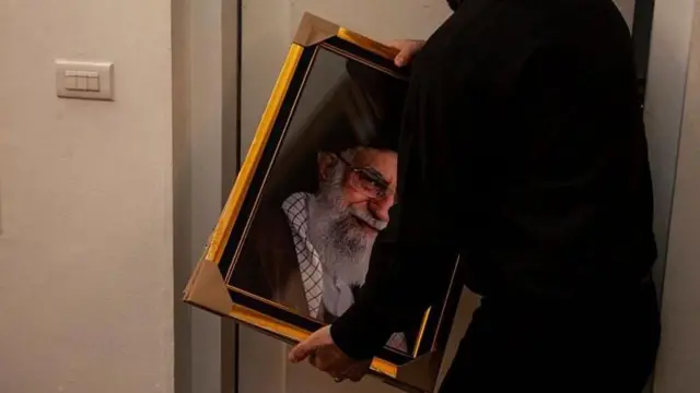 अली ख़ामेनई की तस्वीर ले जाता एक ईरानी अधिकारी