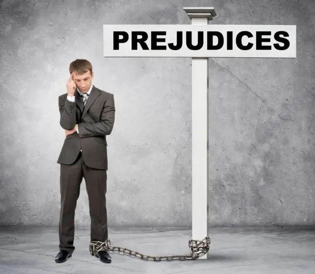 Hombre encadenado a un poste con un cartel que dice "prejuicios".