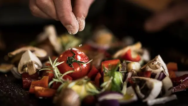 Fotografia de uma mão adicionando sal a uma salada