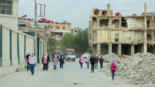 Halep'te çocuklar, savaşta hasar görmüş binaların arasında okula gidiyor.