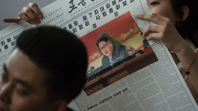 Norcoreanos leyendo un periódico en Corea del Norte, con la foto de Kim Jong-un en la portada.