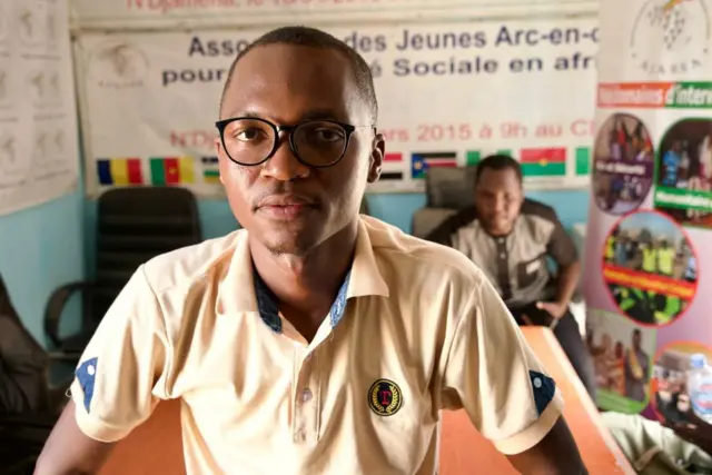 Charles, 28 ans, portant des lunettes et un t-shirt polo beige, regarde à l'intérieurto the camera.