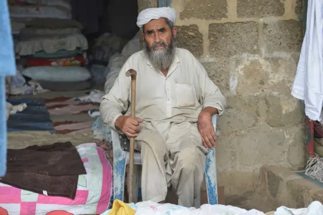 कराची में अपनी दुकान के सामने बैठा एक अफगान नागरिक.