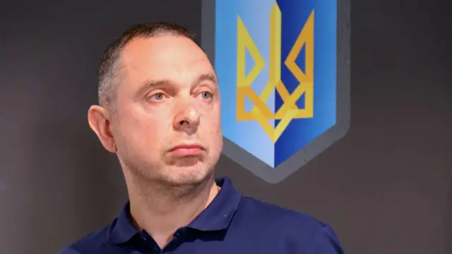 Вадим Гутцайт - мужчина с короткой стрижкой у стены, на которой изображен трезубец