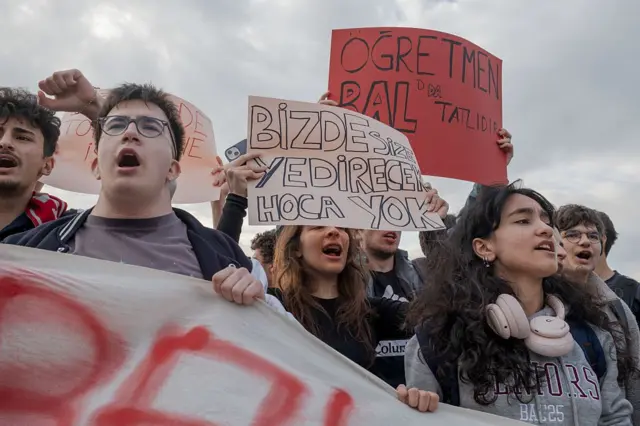 Gençler slogan atıyor, ellerindeki pankartta "Bizde size verecek hoca yok" yazıyor