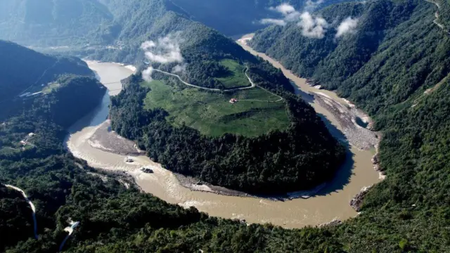 Una vista aérea del río Yarlung Tsangpó y una de sus muchas curvas, mostrando vegetación verde y picos de montañas en la distancia.