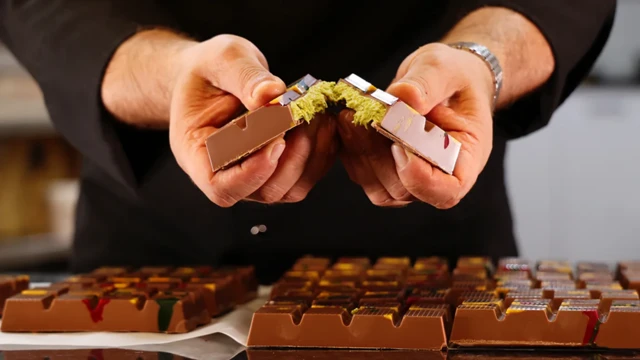 أيدي شاب تقسم لوح من شوكولاتة دبي، وأسفلها عدة ألواح أخرى
