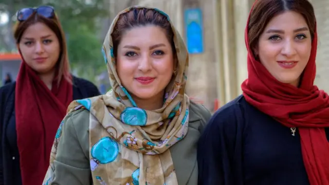 Mlade Iranke, obučene u hidžab, šetaju gradskom ulicom sa mobilnim telefonima u rukama.