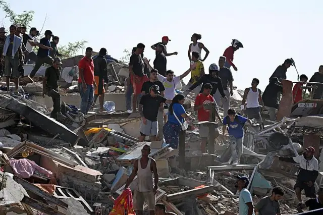 Un grupo de personas busca sobrevivientes mientras otros intentan rescatar sus pertenencias en un edificio derrumbado. 