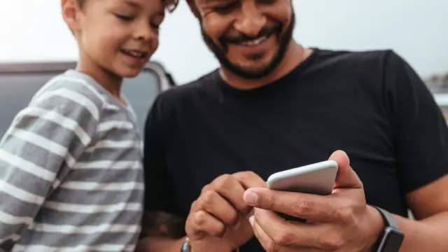 Pai e filho olham sorrindo para celular