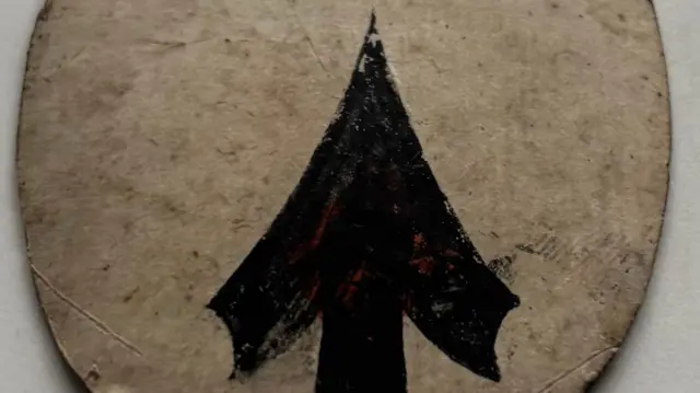 Зворотний бік овальної картки, на якій зображена чорна стрілка, намальована поверх червоного серця.