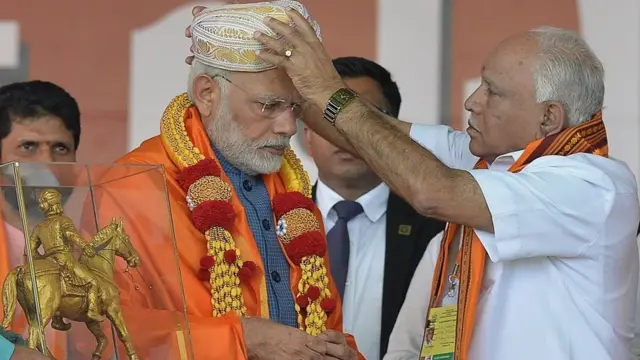 નરેન્દ્ર મોદીને કર્ણાટકી પાઘડી પહેરાવી રહેલા બીજેપીના નેતા યેદિયુરપ્પા