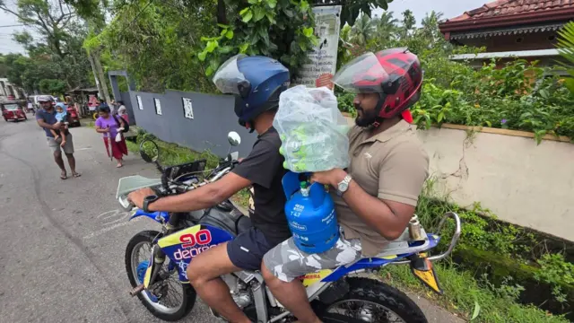 ගම්පහ ප්‍රදේශයේ ගංවතුරට කොටුවී සිටින පිරිස් වෙත යතුරුපැදියක නැගී ආධාර රැගෙන යන අයුරු 