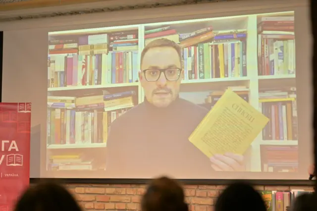 Мирослав Лаюк на екрані зі своєю книжкою в руках