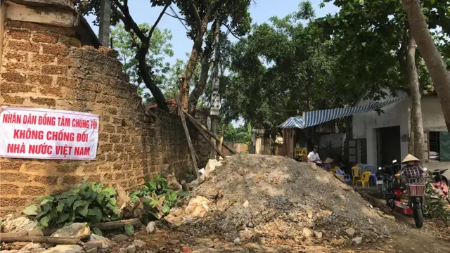 Một người dân đẩy xe đạp điện trên con đường làng có đống gạch đá chắn gần hết bên trong xã Đồng Tâm, huyện Mỹ Đức. Ảnh chụp ngày 20/4/2017.