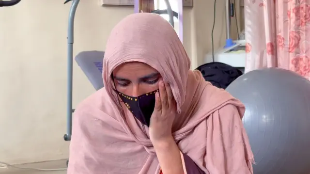 ثریا خپل چپ لاس پرمخ ایښی او ځوړند سر په فکر کې ناسته ده. تر شا یې د فیزیوتراپۍ ځينې وسایل برېښي چې یو هم پکې د لوی توپ په بڼه دی. 
