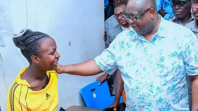 Gomina Caleb Mutfwang ti ipinlẹ Plateau wọ asọ shaati ati sokoto alawọ buluu, n fi ọwọ kan ọbinrin kan to joko sori ibusun nile iwosan, o dirun, to si n rẹrin si gomina