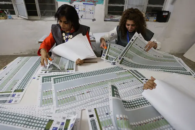 Oy sayan iki kadın görevli ve önlerinde üzerinde çok sayıda aday isminin bulunduğu oy pusulaları 