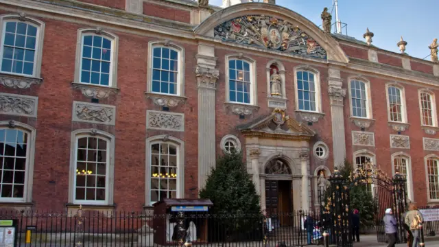 Un gran edificio histórico con una fachada de ladrillos rojos y dos árboles de Navidad en el exterior.