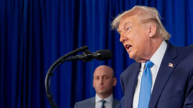 Trump habla frente a un micrófono. En el fondo, se ve al asesor de Seguridad Nacional, Stephen Miller.