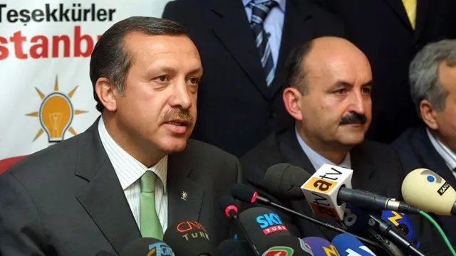 Dönemin AKP lideri Erdoğan, partisinin yaklaşık yüze 35 oy aldığı 3 Kasım 2002 seçimleri sonrası basın açıklaması yapıyor. Yanında partiden farklı isimler var. Önünde birçok mikrofon görülüyor.
