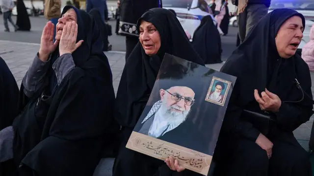Mulheres vestidas com véu preto, chorando e mostrando um retrato de Ali Khamenei