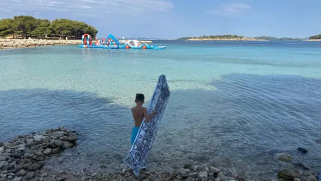 dečak sa dušekom na naduvavanja u plićaku na moru stoji slikan s leđa