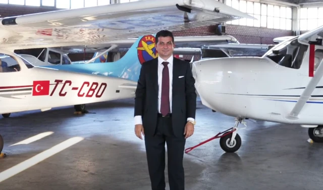 Ünsal Ban uçakların bulunduğu bir hangarda ayakta tek başına poz veriyor