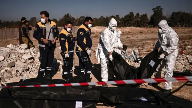 عناصر من الدفاع المدني السوري (الخوذ البيضاء) ينقلون أكياس جثث تحتوي على رفات بشرية تم انتشالها من مقبرة جماعية في دمشق، في 16 ديسمبر/كانون الأول 2024. 