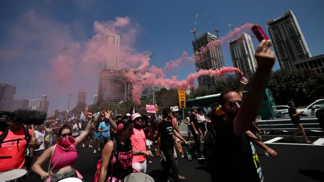 Protesters light red flares and carry drums as they march down a major highway in tel aviv.