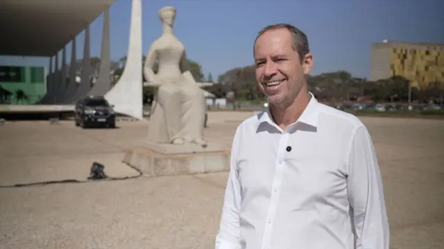 ریکاردو کاپلی که پیراهن سفید به تن دارد، در مقابل مجسمه عدالت در پایتخت برازیلیا ایستاده است.