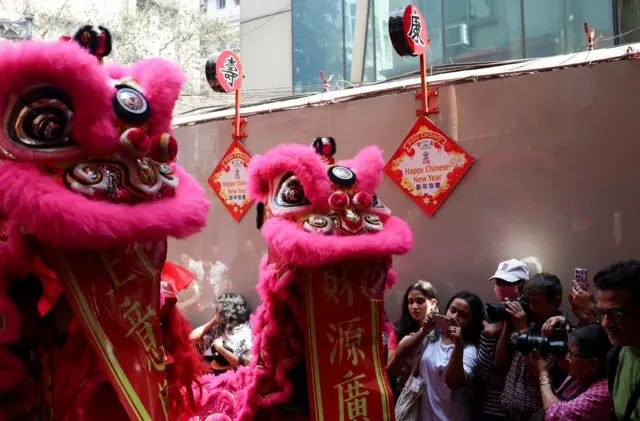 Люди фотографируют розовые матерчатые фигуры, напоминающие драконов