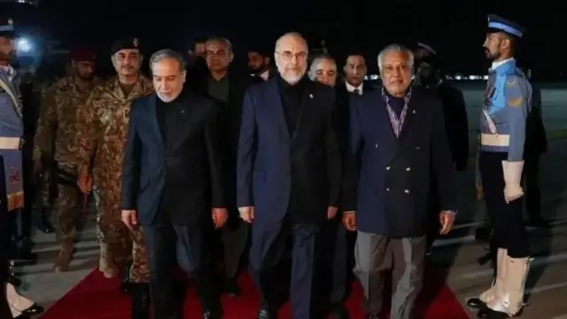 Intumwa za Irani, zirimo umukuru w'inteko ishingamategeko ya Irani Mohammad Bagher Ghalibaf (hagati) na Minisitiri w'ububanyi n'amahanga wa Irani Abbas Araghchi (ibumoso), ubwo zageraga i Islamabad muri Pakistani. Bambaye amakositimu, bari kumwe n'undi mugabo wambaye ikositimu, inyuma yabo hari abantu benshi barimo abasirikare. Baratambuka ku mucyeka utukura. Ifoto yafashwe ari nijoro.