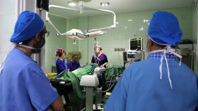 A woman lying on a surgical bed receives plastic surgery in Tehran while two medics look into the operating theatre, on 13 October, 2023