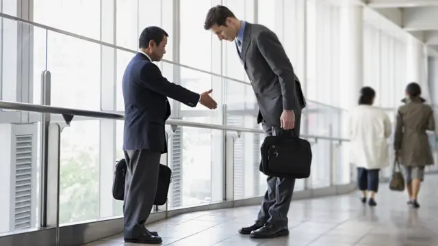 Un ejecutivo japonés ofreciendo la mano a un ejecutivo occidental que se inclina ante él.