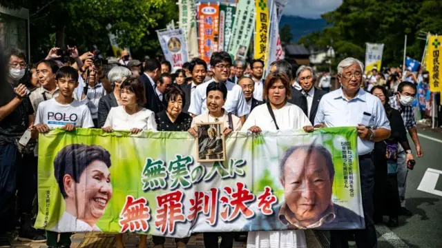 न्यायालयाबाहेर बॅनर घेऊन उभे असलेले हकामाडा यांचे समर्थक