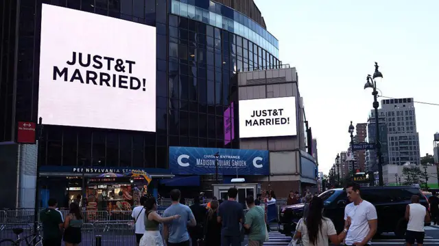 Pessoas assistem a telões gigantes exibindo a mensagem "JUST&T MARRIED!" (T&T de Taylor e Travis) do lado de fora do Madison Square Garden, local onde supostamente aconteceria a cerimônia de casamento da cantora pop Taylor Swift e do atleta profissional Travis Kelce, na cidade de Nova York, em 3 de julho de 2026.