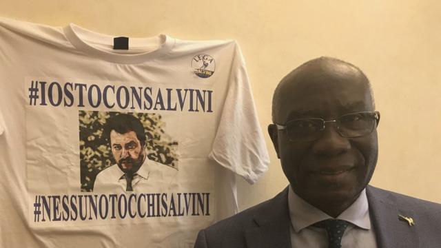 Tony Iwobi debout à côté d'un t-shirt Salvini