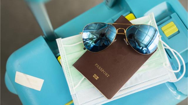 Passaporte, óculos escuros, máscara e mala