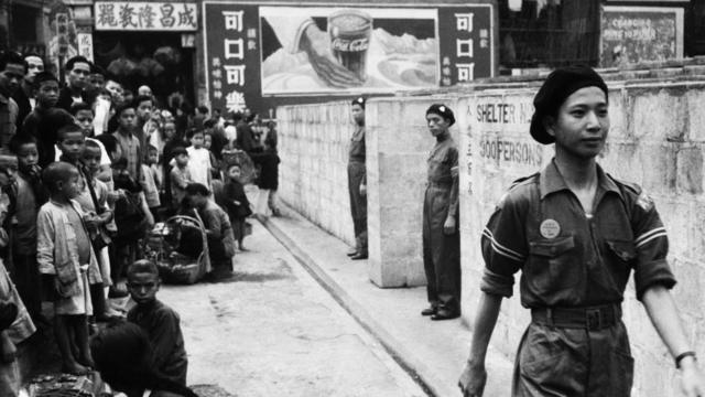 香港街頭某防空洞前小孩圍觀駐守洞口的義勇軍士兵（1941年）