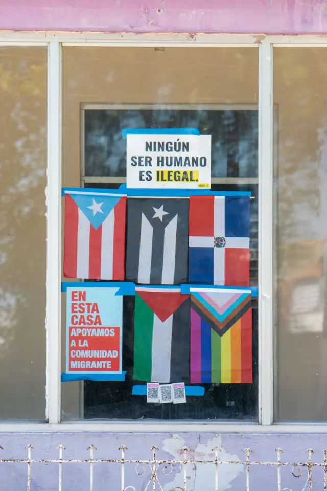 Cartel que dice "ningún ser humano es ilegal" con varias banderas en una puerta de Barrio Obrero, San Juan, Puerto Rico.