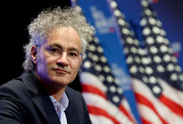 Alex Karp, con unas banderas estadounidenses desenfocadas en el fondo.