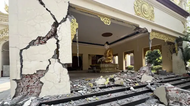 The wall of a pagoda is destroyed showing inside the building with rubble all over the outside steps