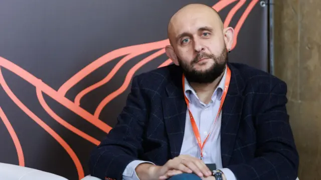 Чоловік у темному піджаку і блакитній сорочці сидить за столом у конференц-залі