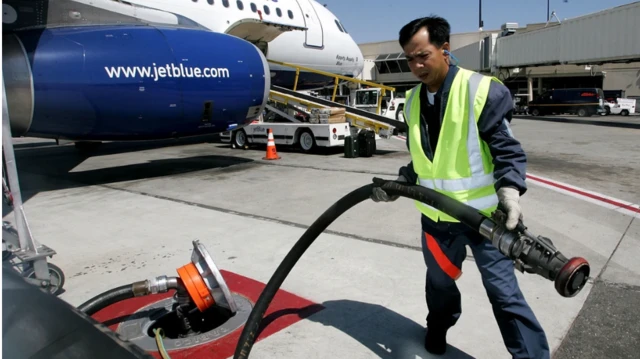 عامل بأحد المطارات يحمل خرطوم مضخة وقود ويقف أمام طائرة ركاب استعدادا لتوصيل الوقود إليها