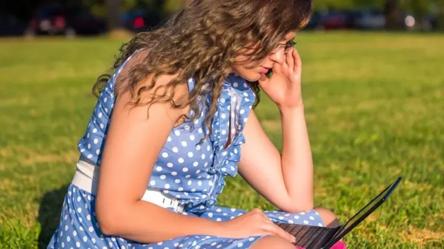 Mulher sentada na grama usando laptop