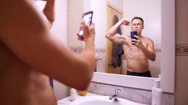 Чоловік фотографує себе, демонструючи м'язи в дзеркалі ванної кімнати - стокова фотографія