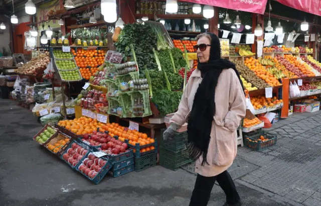 жена пролази поред радње са воћем и поврћем у Техерану